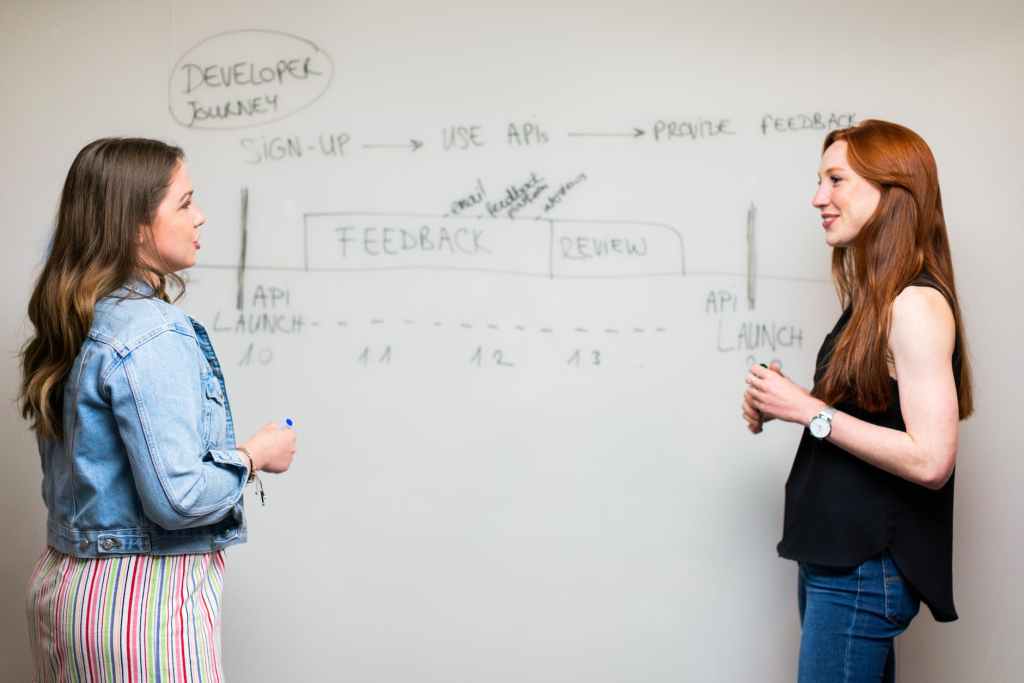 photo of women talking beside whiteboard