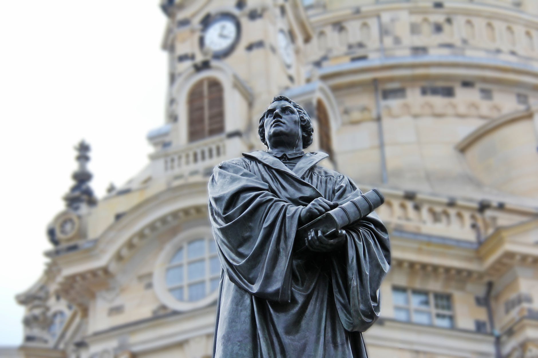 gray concrete statue of man holding book beside brown building