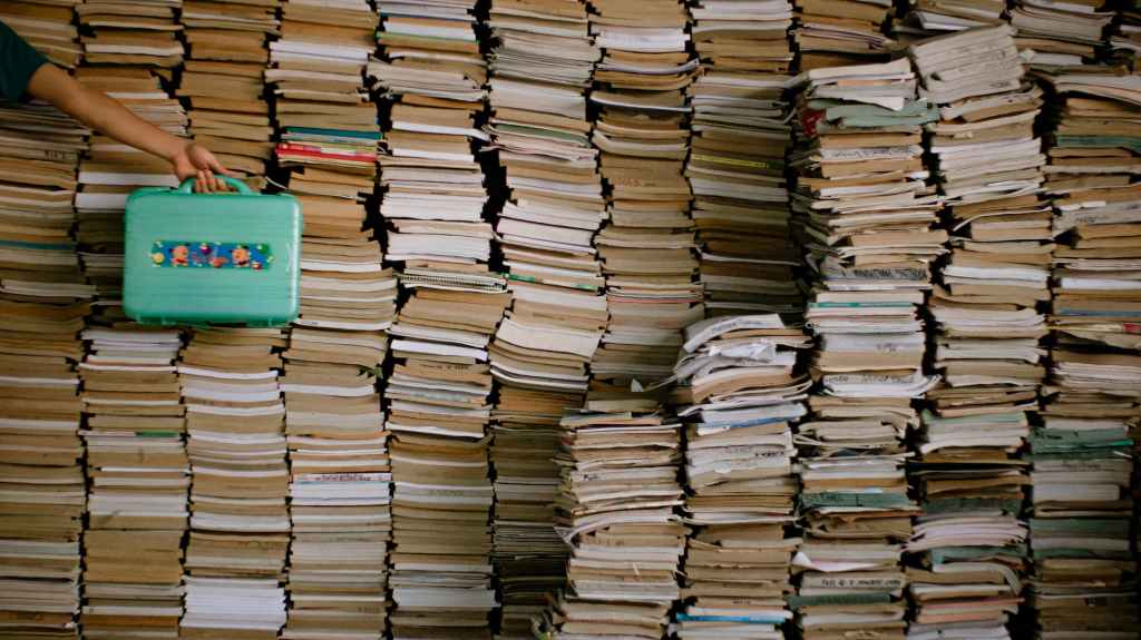 person holding suitcase near stacks of books
