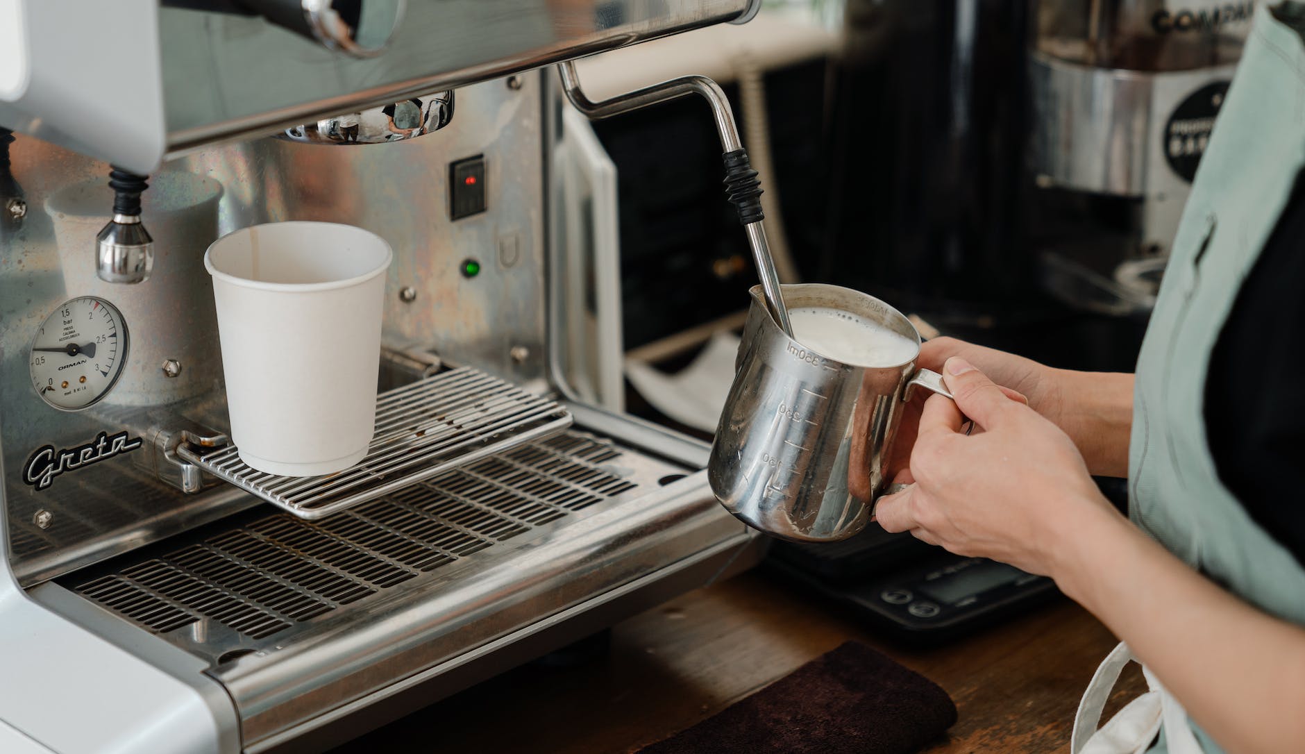 crop barista preparing milk for coffee using coffee machine