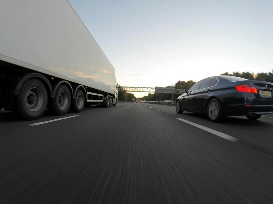 blue infiniti sedan running on road togerther with white freight truck